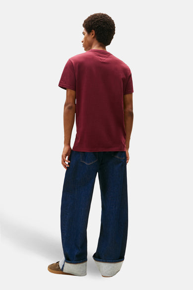 T-shirt rouge à manches courtes de TOMMY JEANS, vu de dos, associé à des jeans larges et des chaussures marrons.