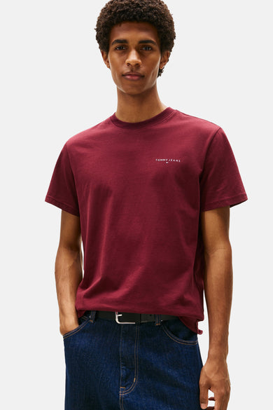 T-shirt rouge à manches courtes de TOMMY JEANS, porté avec des jeans bleus foncés et une ceinture noire.