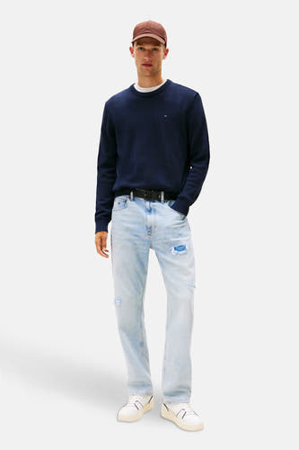 Blauwe trui met ronde hals van TOMMY JEANS, gedragen met lichtblauwe jeans en een bruine pet.
