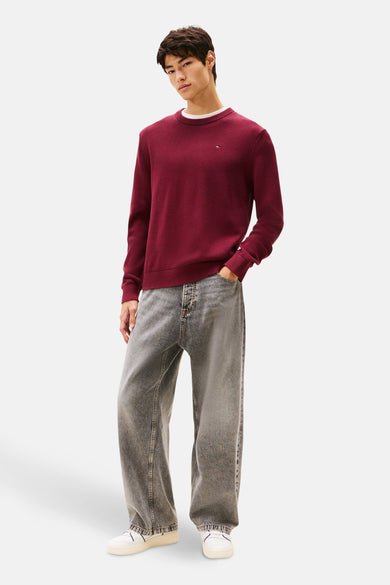 Bordeaux trui met ronde hals van TOMMY JEANS, gedragen met een wit T-shirt en grijze jeans.
