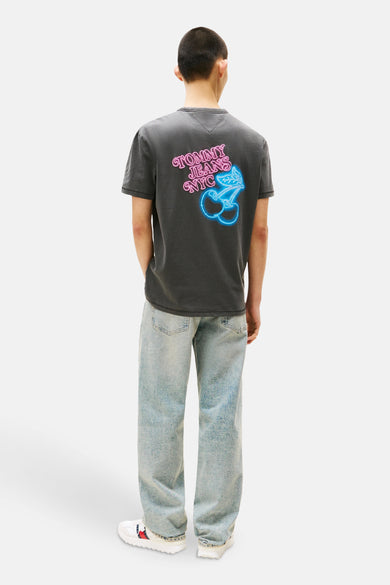 T-shirt gris à manches courtes de TOMMY JEANS, avec un imprimé de cerises néon sur le dos, associé à des jeans légers et des baskets blanches.