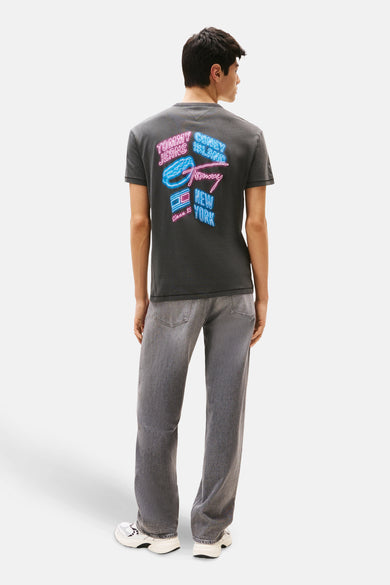 Grijs T-shirt met korte mouwen van TOMMY JEANS, met neon-geïnspireerde print op de achterkant, gecombineerd met grijze jeans en witte sneakers.