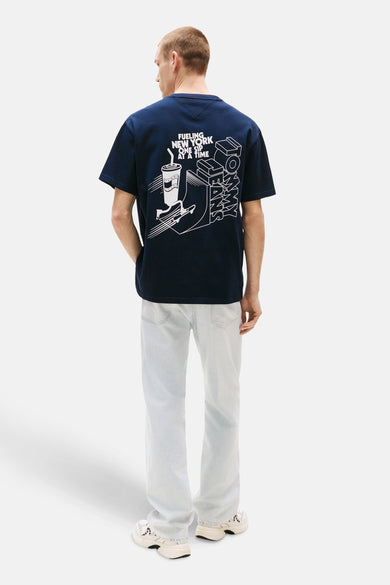 Blauw T-shirt met korte mouwen van TOMMY JEANS, met grafische print op de achterkant, gedragen met lichtblauwe jeans en crèmekleurige sneakers.