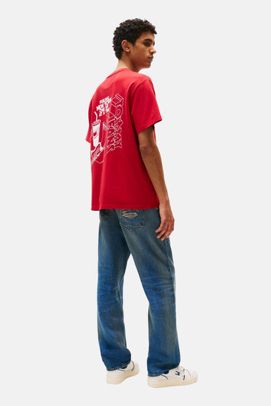 Rood T-shirt met korte mouwen van Tommy Jeans, met een witte print op de rug, gecombineerd met blauwe jeans en witte sneakers.