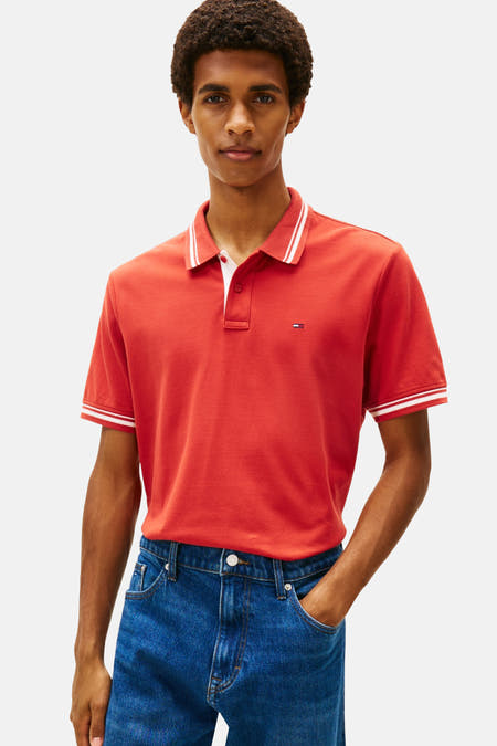 Rode polo met korte mouwen van TOMMY JEANS, afgewerkt met witte accenten op de kraag en mouwen, gedragen met jeans.
