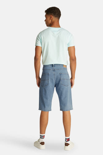 Jean court en denim bleu clair de Tommy Jeans, vu de l'arrière, avec un T-shirt bleu clair et des baskets blanches.