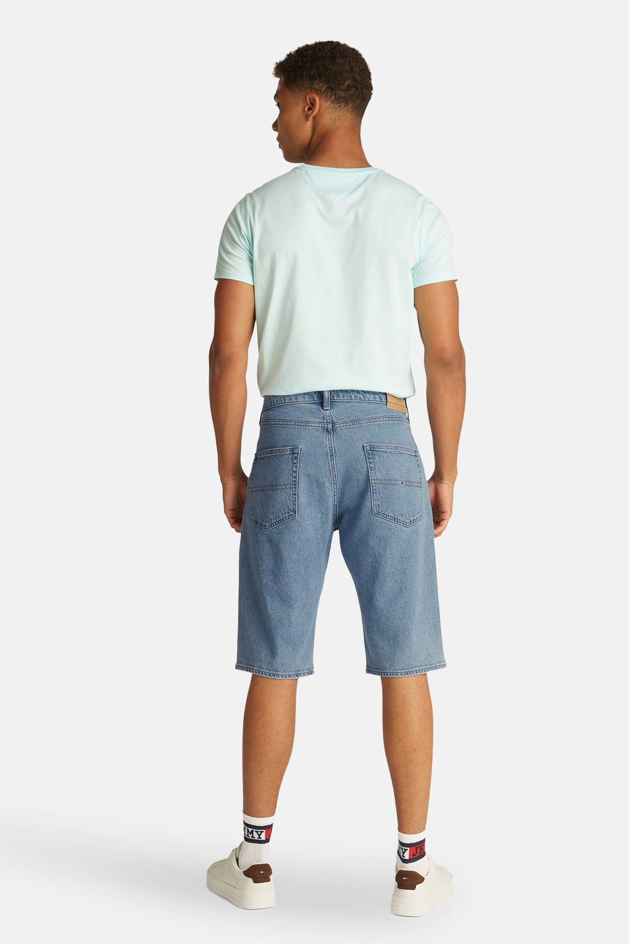 Jean court en denim bleu clair de Tommy Jeans, vu de l'arrière, avec un T-shirt bleu clair et des baskets blanches.