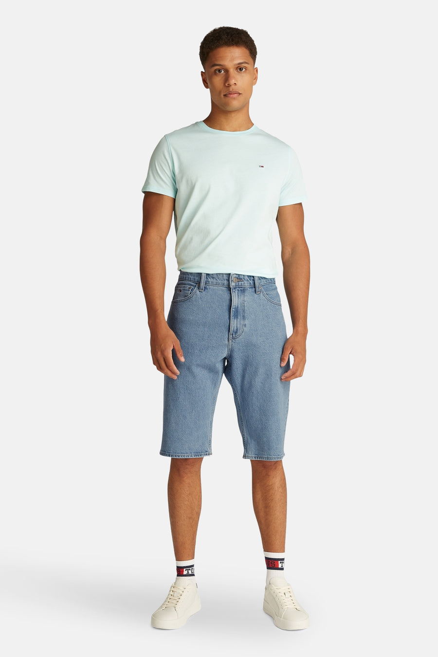Shorts de denim bleu clair de Tommy Jeans, associés à un T-shirt bleu clair et des baskets blanches.