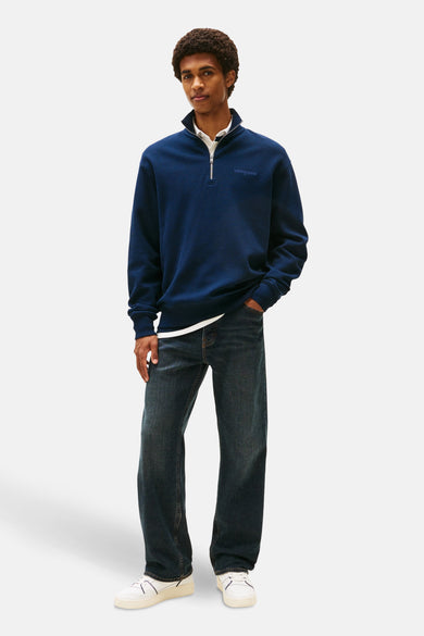 Blauwe sweater van TOMMY JEANS, met halve rits, gedragen met een wit overhemd en donkere jeans.