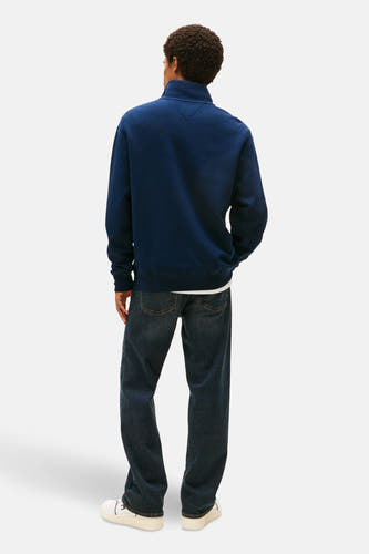 Blauwe sweater van TOMMY JEANS, met lange mouwen, op een model met jeans en witte sneakers.