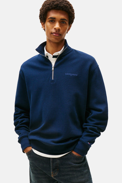 Blauwe sweater van TOMMY JEANS met rits en een geweven textuur, gecombineerd met een wit overhemd en donkere jeans.

