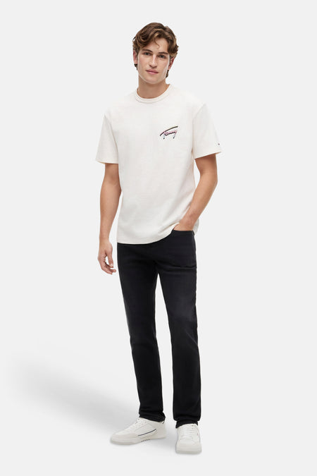 Zwarte slim jeans van TOMMY JEANS, gedragen door een man met een crèmekleurig T-shirt en witte sneakers.
