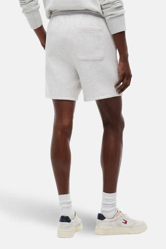 Grijze short van TOMMY JEANS, met achterzak, gecombineerd met witte sokken en crèmekleurige sneakers.
