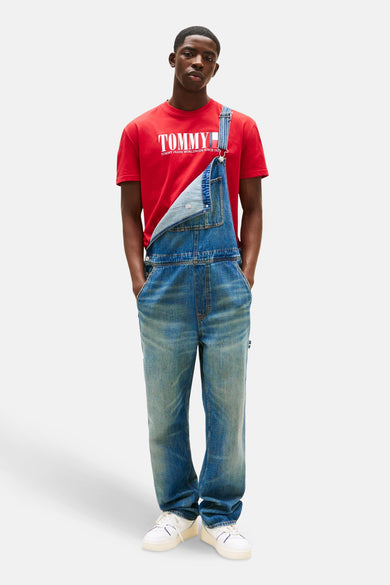 Rood T-shirt met korte mouwen van TOMMY JEANS, gedragen onder een blauwe spijker tuinbroek en witte sneakers.