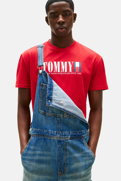 Rood T-shirt met korte mouwen van TOMMY JEANS, gedragen met een denim tuinbroek met de handen in de zakken.