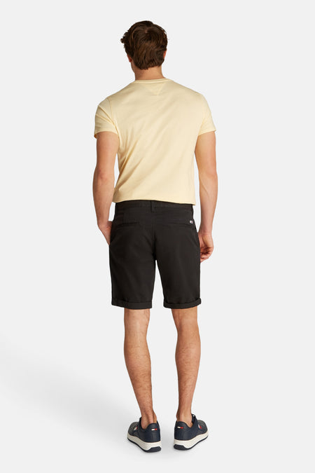 Zwarte short van TOMMY JEANS, achterkant met riemlussen en opgerolde zoom, gedragen met een geel T-shirt en blauwe sneakers.
