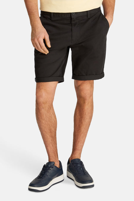 Zwarte short van TOMMY JEANS, met opgerolde pijpen en gedragen met blauwe sneakers.