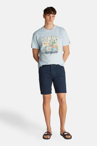 Blauwe short van TOMMY JEANS, gedragen met een lichtblauw T-shirt met print en zwarte slippers.