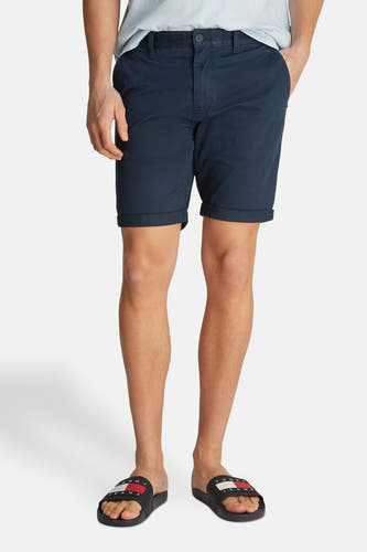 Blauwe short van TOMMY JEANS, met omgeslagen zoom, gedragen met teenslippers.
