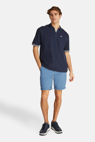 Short bleu de TOMMY JEANS, avec des revers relevés, associé à un poloshirt bleu marine et des chaussures.