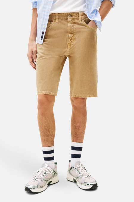 Jean court beige de TOMMY JEANS, avec une texture distinctive, associé à un chemisier rayé bleu et une casquette bleu marine.