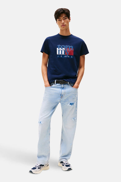 T-shirt bleu à manches courtes de TOMMY JEANS, avec logo sur la poitrine, porté avec des jeans légers et des baskets.