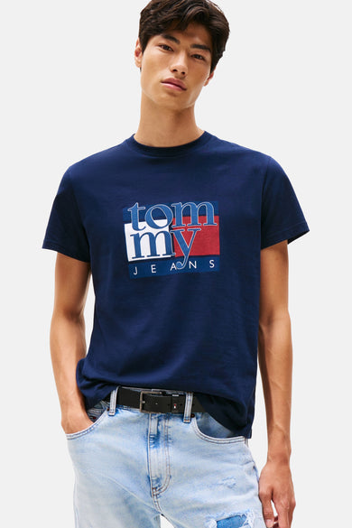 T-shirt bleu à manches courtes de TOMMY JEANS, avec impression de logo, porté avec des jeans et une ceinture.