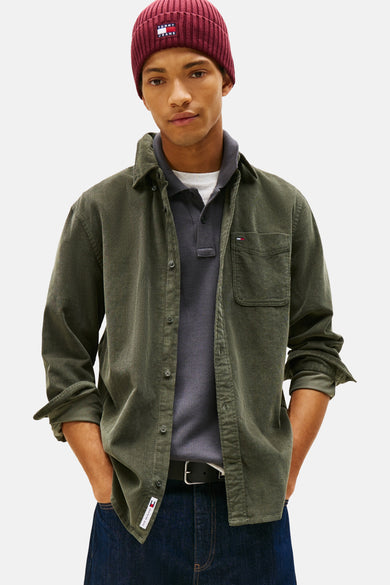 Groen hemd van TOMMY JEANS, met lange mouwen en een borstzakje, gedragen over een donkergrijze polo en een donkerblauwe jeans.