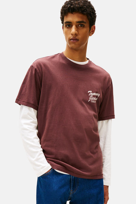 Bruin T-shirt met korte mouwen van Tommy Jeans, gedragen over een wit shirt met lange mouwen, en blauwe jeans.