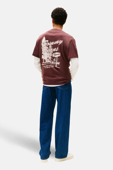 T-shirt brun à manches courtes de TOMMY JEANS, avec une impression blanche sur le dos, associé à un t-shirt blanc à manches longues et des jeans bleus.