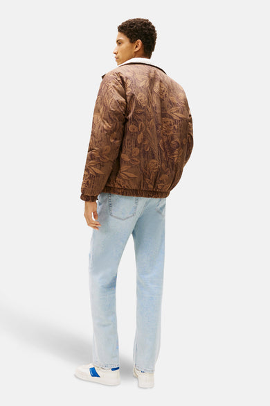Bruine korte jas van TOMMY JEANS met bloemmotief, gecombineerd met lichtblauwe jeans en witte sneakers.