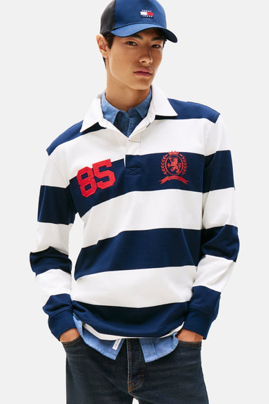 Blauwe sweater van TOMMY JEANS, met strepen, rode applicaties en een blauw petje.
