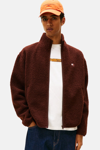 Bruine jas van TOMMY JEANS met een sherpa-textuur, gedragen over een wit T-shirt en blauwe jeans.