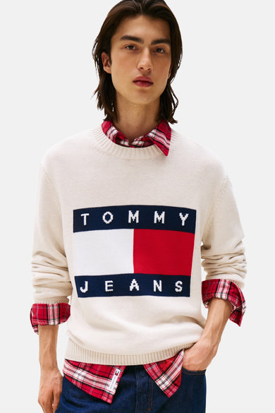 Ecrukleurige trui met ronde hals van Tommy Jeans, met een rechthoekige logoprint en gedragen over een rood geruit overhemd.
