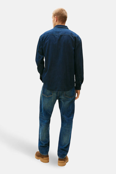 Donkerblauw denim jeanshemd van TOMMY JEANS, gezien van achteren, gecombineerd met jeans en bruine schoenen.
