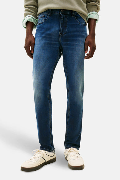 Donkerblauwe tapered jeans van TOMMY JEANS, met casual schoenen en een groene trui.
