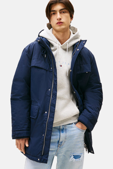 Man met blauwe jas en grijze hoodie, spijkerbroek met gaten, witte achtergrond.