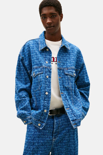 Jeansjas van midblauw denim van TOMMY JEANS, met een all-over logo print, gedragen over een wit T-shirt en zwarte riem.
