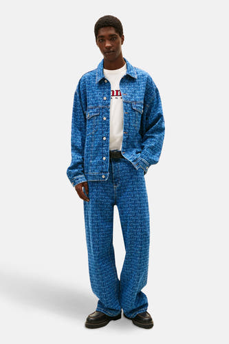 Denim jeansjas van TOMMY JEANS met logoprint over de gehele jas, gecombineerd met een witte T-shirt en bijpassende jeans.
