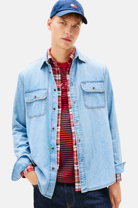 Jeanshemd in middenblauw denim van TOMMY JEANS, met lange mouwen en borstzakken, gedragen over een gestreept shirt.