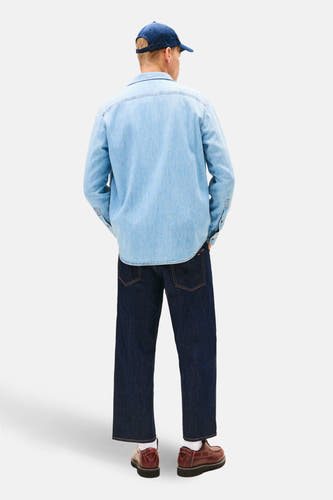 Denim overhemd in middenblauw van TOMMY JEANS, met lange mouwen, gecombineerd met donkere jeans en bruine schoenen.