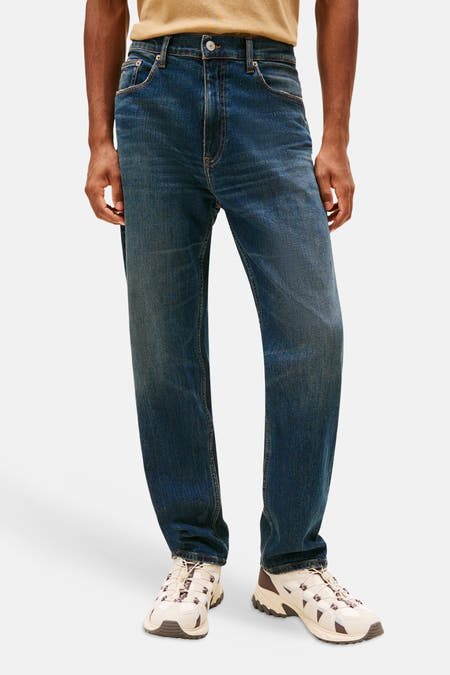 Tapered jeans van donkerblauw denim van Tommy Jeans, met een normale taille en beige-bruine sneakers.
