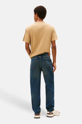 Tapered jeans van donkerblauw denim van TOMMY JEANS, met een bruine leren riem en crèmekleurige schoenen.
