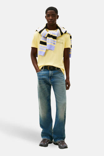 T-shirt jaune à manches courtes de TOMMY JEANS, avec un pull rayé sur les épaules et des jeans bleus.