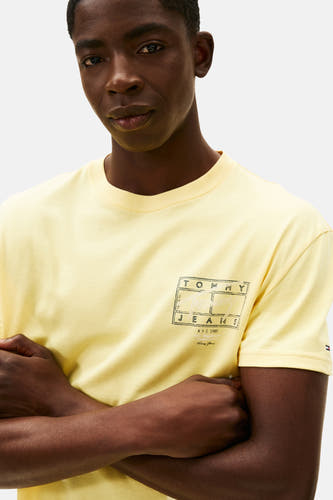 T-shirt jaune à manches courtes de TOMMY JEANS, avec logo sur la poitrine et bras croisés.