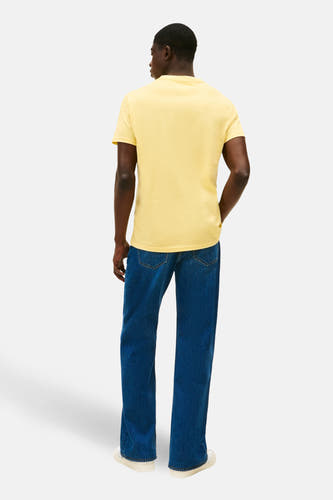 Geel T-shirt met korte mouwen van TOMMY JEANS, met effen design, gedragen met blauwe jeans en witte sneakers, gezien van achteren.
