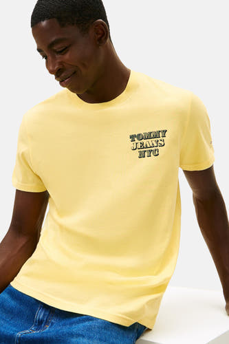Geel T-shirt met korte mouwen van TOMMY JEANS, met tekstlogo op de borst en gedragen met een blauwe jeans.
