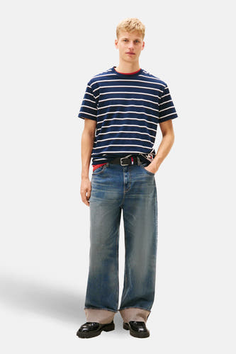 Blauw gestreept T-shirt met korte mouwen van TOMMY JEANS, met rode accenten aan de halslijn, gecombineerd met wijde jeans en zwarte schoenen.
