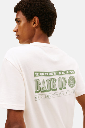 Een man met een wit T-shirt met groene 'Tommy Jeans Bank Of NYC'-opdruk.