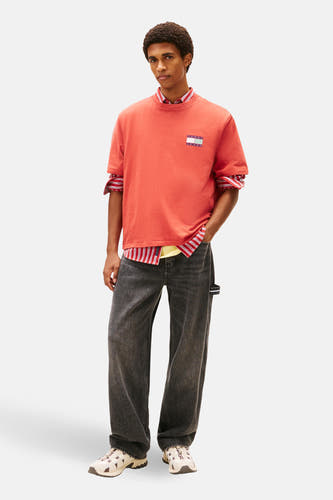 Rood T-shirt met korte mouwen van Tommy Jeans, met een gestreept overhemd eronder en wijde, donkergrijze jeans.
